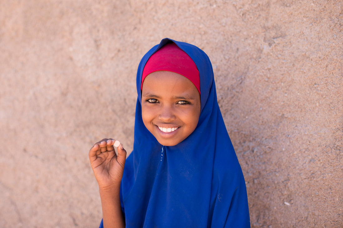 A young girl smiles as she holds up a deworming pill.