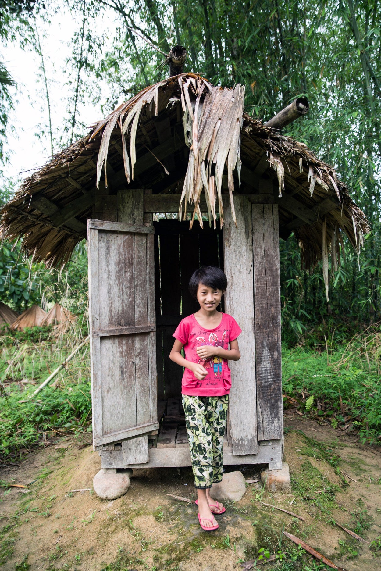 A girl stands in front of her latrine.