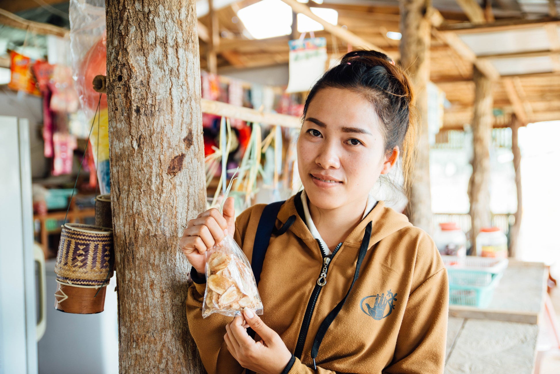 a woman in a brown sweatshirt holding up a bag of banana chips