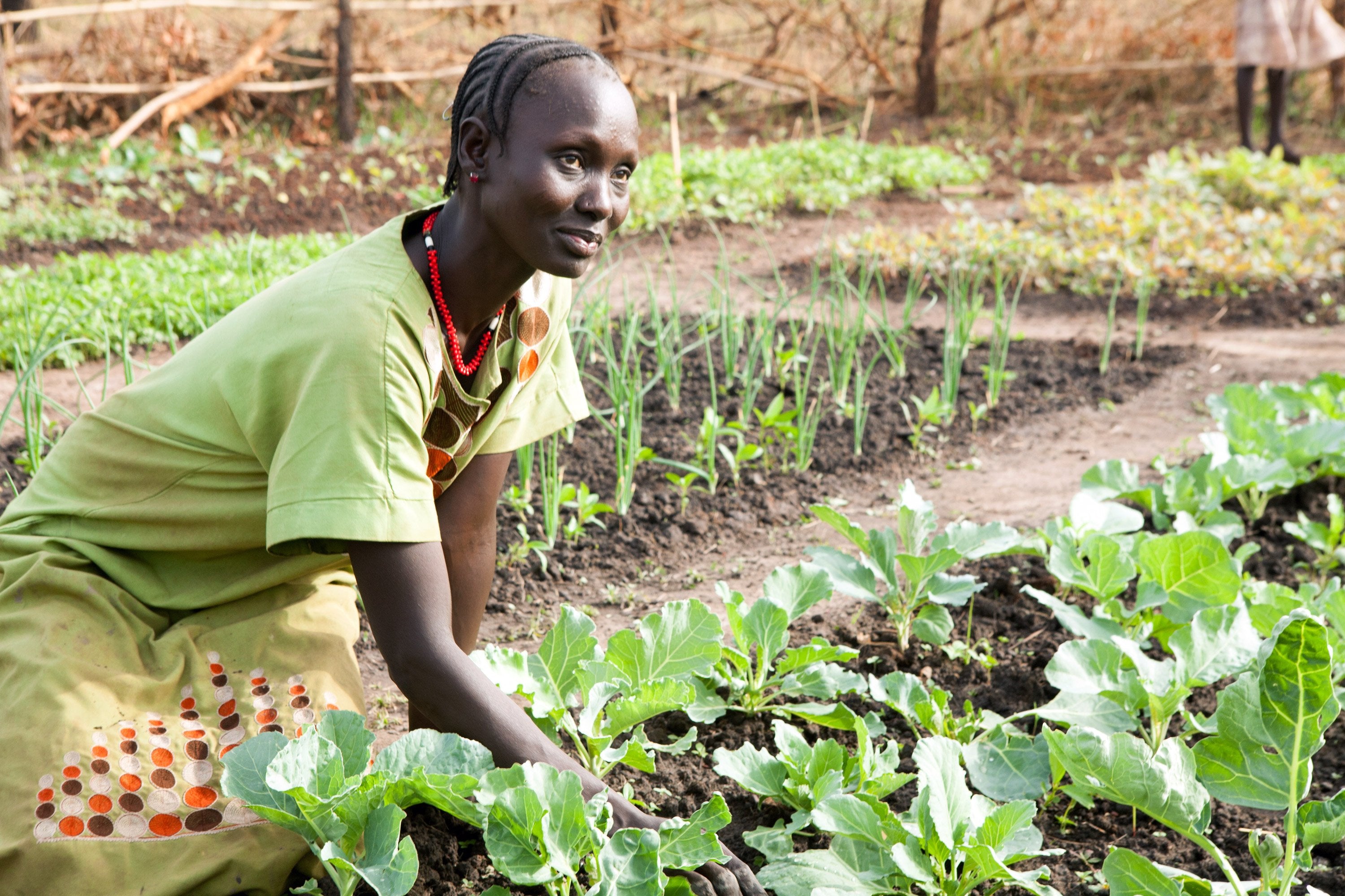 A woman smiles as she shows off the produce from her vegetable garden.